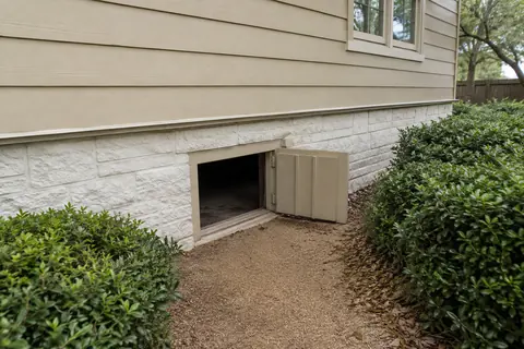 Open framed crawlspace access door in a low masonry wall with a clear dry approach, illustrative image