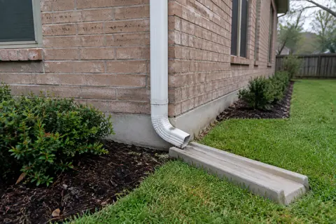 Downspout at the base of a brick house, illustrative image