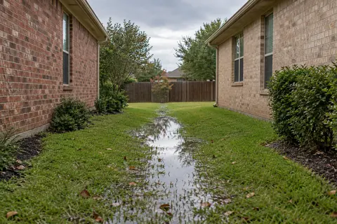 Shallow rainwater pooling along a grassy side yard between two brick homes